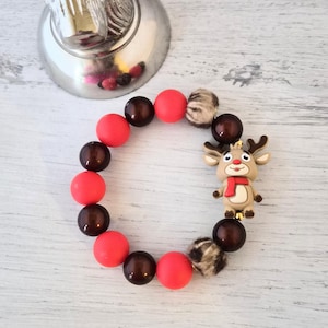 Könnte beinhalten: Ein festliches Armband mit abwechselnd roten und dunkelbraunen Perlen, Akzenten aus Kunstfell und einem Rentier-Anhänger. Das Rentier hat einen roten Schal und ein Geweih. Das Armband ist für einen bequemen Sitz konzipiert.