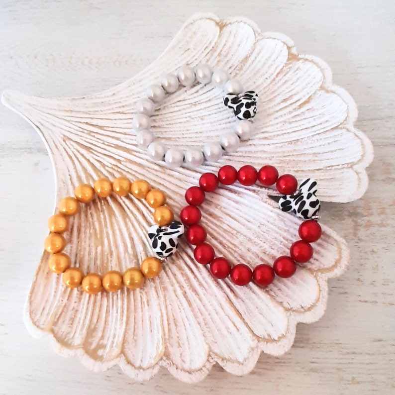 May include: Three bracelets with animal print charms. The bracelets are made of gold, red, and white beads.