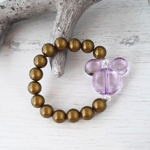 May include: A brown beaded bracelet with a purple Mickey Mouse charm. The bracelet is made of round beads and the charm is made of faceted glass.