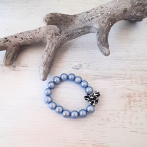 May include: A light blue beaded bracelet with a black and white patterned charm. The bracelet is made of round, smooth beads.