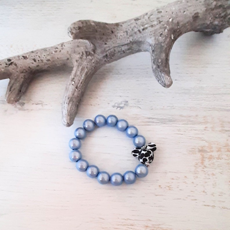 May include: A light blue beaded bracelet with a black and white patterned charm. The bracelet is made of round, smooth beads.