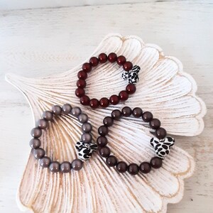 May include: Three beaded bracelets with animal print charms. The bracelets are in shades of brown, gray, and burgundy.