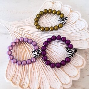 May include: Three bracelets with different colored beads and a patterned heart charm. The bracelets are purple, green, and dark purple.