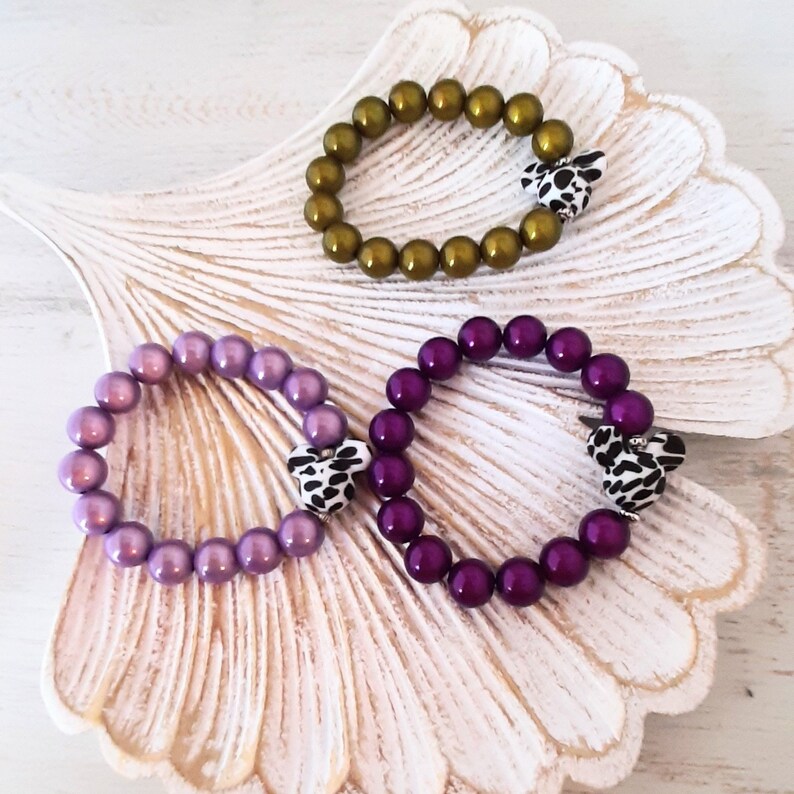 May include: Three bracelets with different colored beads and a patterned heart charm. The bracelets are purple, green, and dark purple.