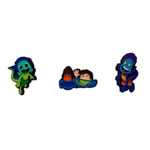 May include: Three cartoon character charms featuring a blue and green creature, two children in a blue raft, and a blue and purple creature with a yellow shirt.