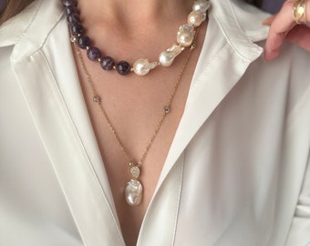 May include: A layered necklace with a large baroque pearl pendant. The top layer is a multi-strand necklace with amethyst beads and white baroque pearls. The bottom layer is a delicate gold chain with a small pearl pendant.