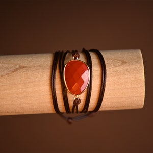 May include: A brown leather wrap bracelet with a red gemstone pendant.