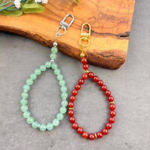 May include: Two beaded wristlet keychains. One features light green round beads with silver-toned spacers and a silver-toned lobster clasp. The other features red round beads with gold-toned spacers and a gold-toned lobster clasp.