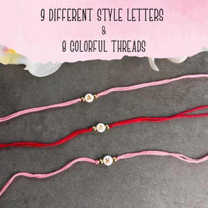 May include: Three bracelets made of thin thread in shades of pink and red. Each bracelet features a single white circular bead with a gold letter, flanked by two small gold-toned metallic beads. The text 9 DIFFERENT STYLE LETTERS & 8 COLORFUL THREADS is visible.