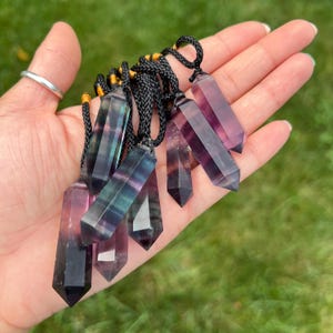 May include: A collection of rainbow fluorite crystal pendants on black cords. The crystals are pointed and have a variety of colors, including purple, green, and black.