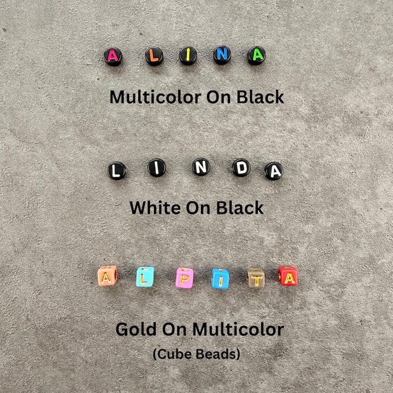 May include: Three rows of alphabet beads. The first row spells ALINA with multicolored letters on black beads. The second row spells LINDA with white letters on black beads. The third row spells ALPITA with gold letters on multicolored cube beads.