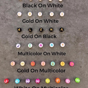 May include: Six rows of round alphabet beads displaying various color combinations: black letters on white, gold on white, gold on black, multicolor on white, gold on multicolor, and white on multicolor. Each row includes text labels identifying the style.