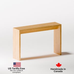 May include: A small, rectangular wooden table with a light brown finish. The table has a simple, modern design with a flat top and two rectangular legs. The table is approximately 30 inches long, 10 inches wide, and 30 inches tall.