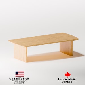 May include: A light-coloured wooden coffee table with a rectangular top and two supporting side panels. The table has a simple, modern design and is made of light-coloured wood. The table is approximately 91 cm long and 46 cm wide.