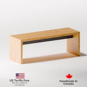 May include: A rectangular wooden bench with a light brown top and sides, featuring a dark band along the underside. The bench is made of light-colored wood and has a minimalist design. The bench is approximately 48 inches long.