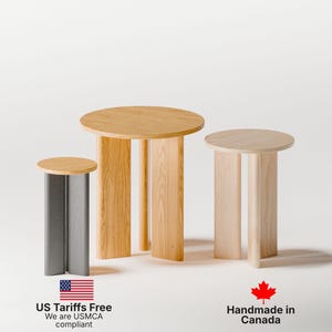May include: Three wooden side tables of varying heights. The tables have round tops and rectangular legs. One table is gray with a light wood top. The other two tables are light wood. The tables are USMCA compliant.