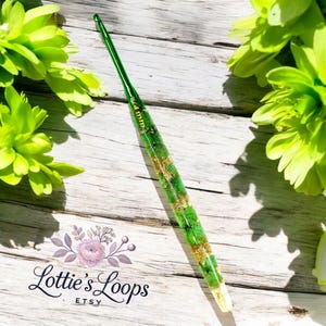 May include: A green crochet hook with gold glitter and four-leaf clover accents. The hook is 4 mm in size.