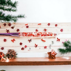 May include: A purple and white Christmas-themed glass tube filled with red and white candy canes. The tube is lying on a wooden surface with red and white decorations.