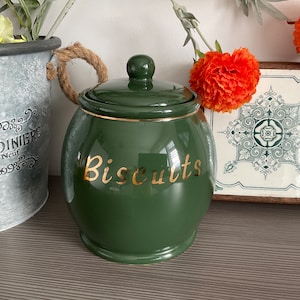 Może przedstawiać: Zielony ceramiczny pojemnik na ciasteczka z złotą pokrywką i złotym napisem "Biscuits".