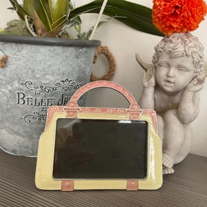 May include: A yellow and pink ceramic picture frame shaped like a handbag with a handle. The frame has a black background and is ready to hold a photo.