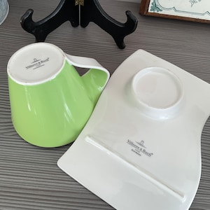 May include: A green and white ceramic teacup and saucer set with the Villeroy & Boch logo. The cup has a unique shape and the saucer is curved.
