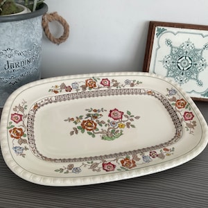 May include: A white oval serving platter with a floral design in shades of red, orange, yellow, green, and blue. The platter has a raised rim and a scalloped edge.
