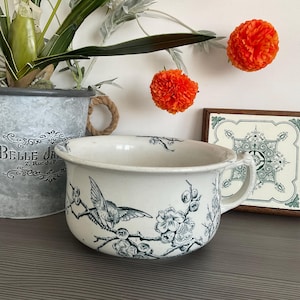 Puede incluir: Bote de cerámica blanca con un diseño floral azul y blanco con pájaros. El bote tiene dos asas y el texto "Belle Ja 2, Rue du Pont" es visible en el lateral.