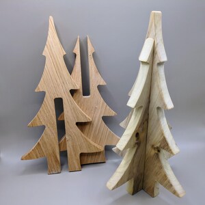 May include: A collection of wooden Christmas tree decorations. The trees are crafted from light-coloured wood, displaying the natural grain. Designs vary from simple outlines to layered, three-dimensional forms, ideal for festive displays.