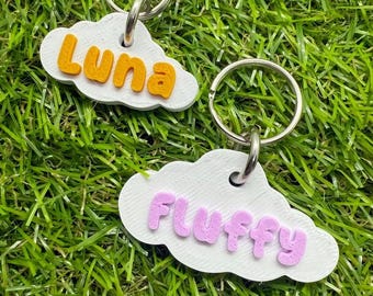 Può includere: Due portachiavi a forma di nuvola con anelli argentati. Uno ha il nome "Luna" in lettere arancioni, l'altro "Fluffy" in rosa. Entrambi sono bianchi. Ideale per i proprietari di animali.