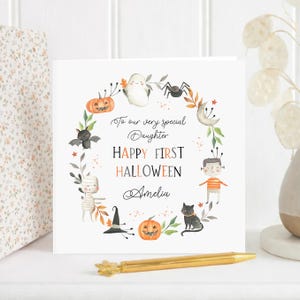 Personalised first Halloween card for a daughter featuring a cute watercolour ghost, pumpkin, bat, mummy, spider, black cat and witch's hat. The card reads Happy First Halloween and is personalised for a very special daughter granddaughter son grandson