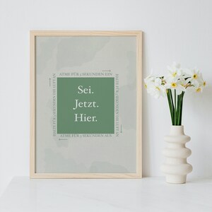 K&ouml;nnte beinhalten: Ein gerahmter Druck mit gr&uuml;nem Hintergrund und wei&szlig;em Text, der "Sei. Jetzt. Hier." lautet. Der Text ist von Pfeilen umgeben, die in entgegengesetzte Richtungen zeigen, mit den Worten "Atme f&uuml;r 3 Sekunden ein" und "Halte f&uuml;r 3 Sekunden die Luft an".