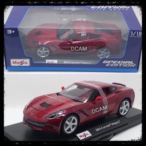 May include: A red 2014 Corvette Stingray die-cast model car, 1/18 scale, displayed in its original box and on a black base. The model features detailed design and silver wheels. The box reads "Special Edition".
