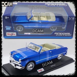 May include: A blue 1949 Ford convertible diecast model car in 1/18 scale. The car is on a black display stand with the Maisto logo. The box shows the car in the same pose with the text "DCAM Special Edition 1/18 Scale" on the box.