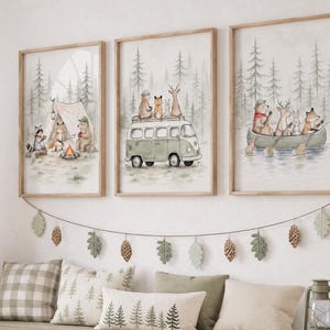 May include: Three framed watercolor prints featuring woodland animals camping, driving a van, and canoeing in a forest. Below the prints hangs a garland of felt leaves and pinecones above a long wooden storage bench with white bins and cushions.