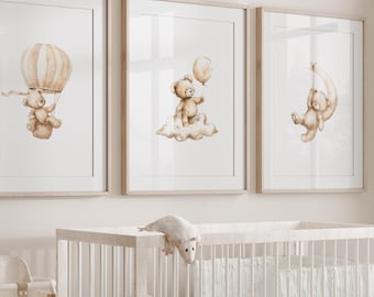 May include: Three framed watercolor prints of teddy bears in a nursery setting. The prints feature a teddy bear in a hot air balloon, a teddy bear on a cloud, and a teddy bear hanging from a crescent moon. The prints are hung above a white crib with a white mattress and a white crib sheet.