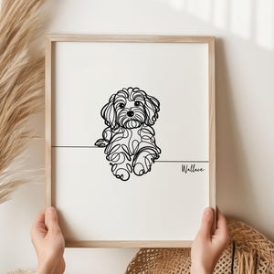 May include: A framed print with a minimalist line drawing of a dog. The black artwork is set against a white background, with the dog's name, "Wallace," written in cursive. The frame is made of light-coloured wood.