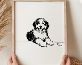 Könnte beinhalten: Ein gerahmter Schwarz-Weiß-Kunstdruck eines Bernedoodle-Welpen. Das Kunstwerk zeigt einen minimalistischen Stil mit der Umrisslinie des Welpen und dem Namen "Monty" in Schreibschrift. Der Rahmen hat eine helle Holzfarbe.