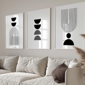 May include: A white sectional sofa with brown throw cushions sits in a living room with a wooden coffee table and a beige rug. Three black and white abstract art prints hang on the wall above the sofa.