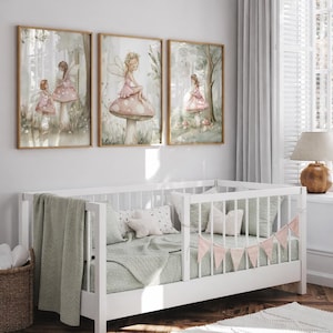 May include: Three framed art prints featuring watercolor illustrations of fairies in a forest setting. The fairies are depicted in pink dresses, some seated on mushrooms. The artwork is displayed above a white crib with green bedding and a pink banner.