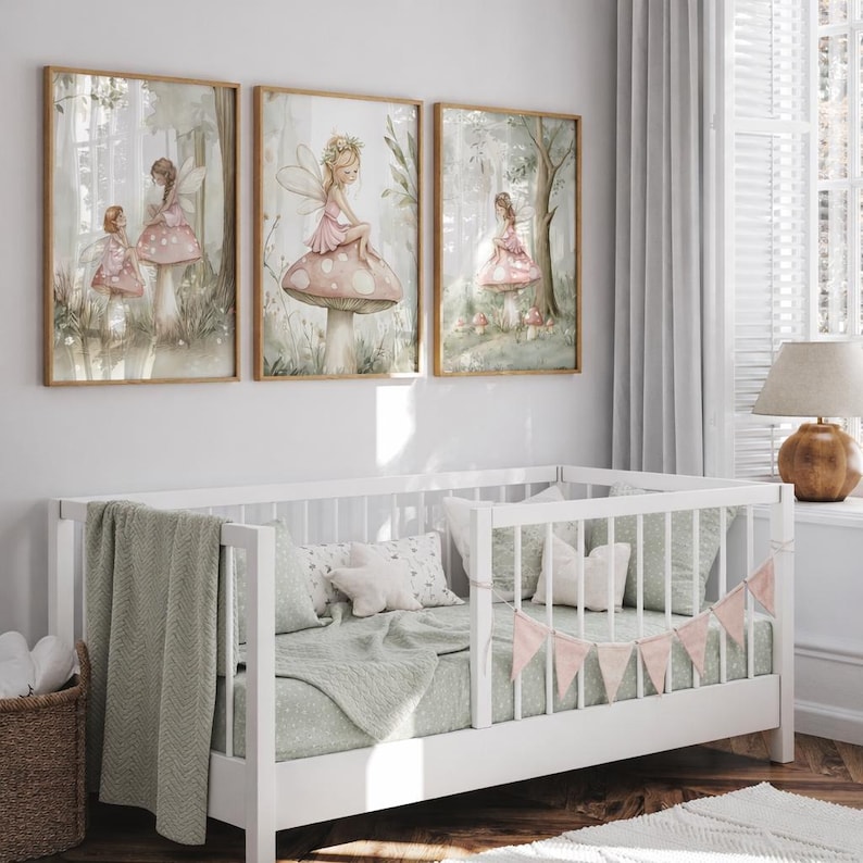 May include: Three framed art prints featuring watercolor illustrations of fairies in a forest setting. The fairies are depicted in pink dresses, some seated on mushrooms. The artwork is displayed above a white crib with green bedding and a pink banner.