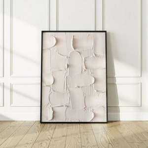 Peut inclure: Une peinture abstraite encadr&eacute;e avec une palette de couleurs textur&eacute;e, blanche et cr&egrave;me. La peinture est dans un cadre noir et est accroch&eacute;e &agrave; un mur blanc.