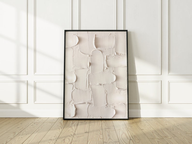 Peut inclure: Une peinture abstraite encadr&eacute;e avec une palette de couleurs textur&eacute;e, blanche et cr&egrave;me. La peinture est dans un cadre noir et est accroch&eacute;e &agrave; un mur blanc.