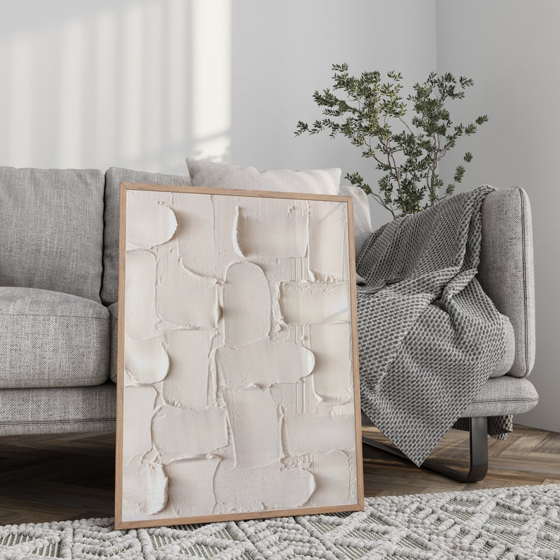 Peut inclure: Une peinture abstraite encadr&eacute;e avec un motif textur&eacute; blanc. La peinture est accroch&eacute;e &agrave; un mur dans un salon avec un canap&eacute; gris et une couverture.