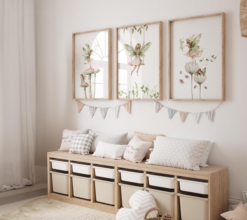 May include: Three framed watercolor prints featuring fairies in a whimsical setting. The prints depict fairies on mushrooms, swings, and flowers, with soft green and pink hues. The frames are light brown, and the overall theme is a children's room.