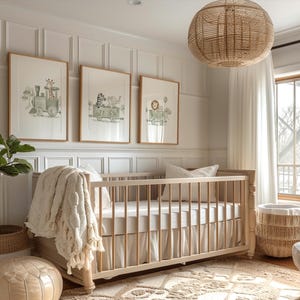 May include: A light-colored wooden crib with a white skirt and bedding, draped with a cream-colored textured throw blanket. Above the crib hang three framed watercolor prints featuring animals riding in a train, set against a white paneled wall.