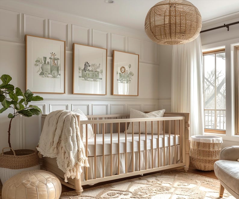 May include: A light-colored wooden crib with a white skirt and bedding, draped with a cream-colored textured throw blanket. Above the crib hang three framed watercolor prints featuring animals riding in a train, set against a white paneled wall.