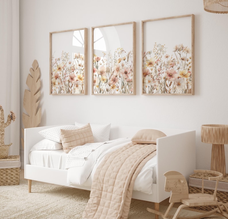 Puede incluir: Tres impresiones enmarcadas de ilustraciones florales de acuarela en tonos beige, melocot&oacute;n y marr&oacute;n. Las impresiones est&aacute;n colgadas en una pared blanca sobre una cama individual blanca con una colcha y almohadas beige.