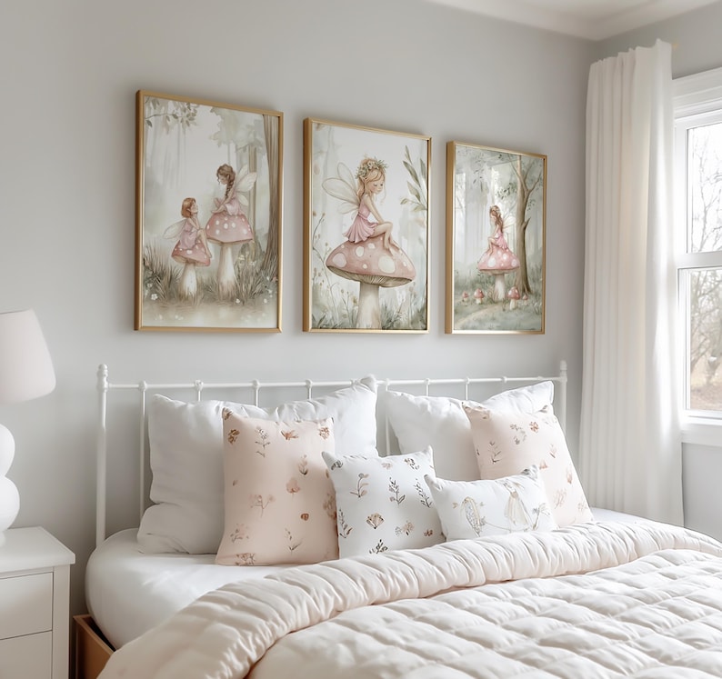 May include: Three framed watercolor art prints featuring fairies in a whimsical forest setting. The prints have gold frames and depict fairies on mushrooms. The bed below has white bedding and decorative pillows with floral patterns.