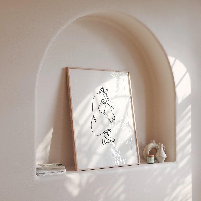 K&ouml;nnte beinhalten: Ein gerahmtes Schwarzwei&szlig;-Linienbild eines Pferdekopfes mit dem Wort "Dream" darunter. Der Rahmen ist aus hellem Holz und der Hintergrund ist eine hellbeige Wand.