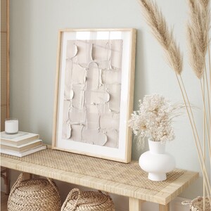 Peut inclure: Un banc en bois clair avec un dessus en rotin tiss&eacute;, deux paniers tiss&eacute;s et un vase en c&eacute;ramique blanche avec des fleurs blanches s&eacute;ch&eacute;es. Un tableau abstrait encadr&eacute; avec un fond beige est accroch&eacute; au mur derri&egrave;re le banc.